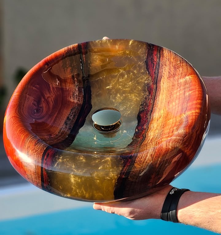 Lavabo de madera y resina dorada sostenido junto a una piscina